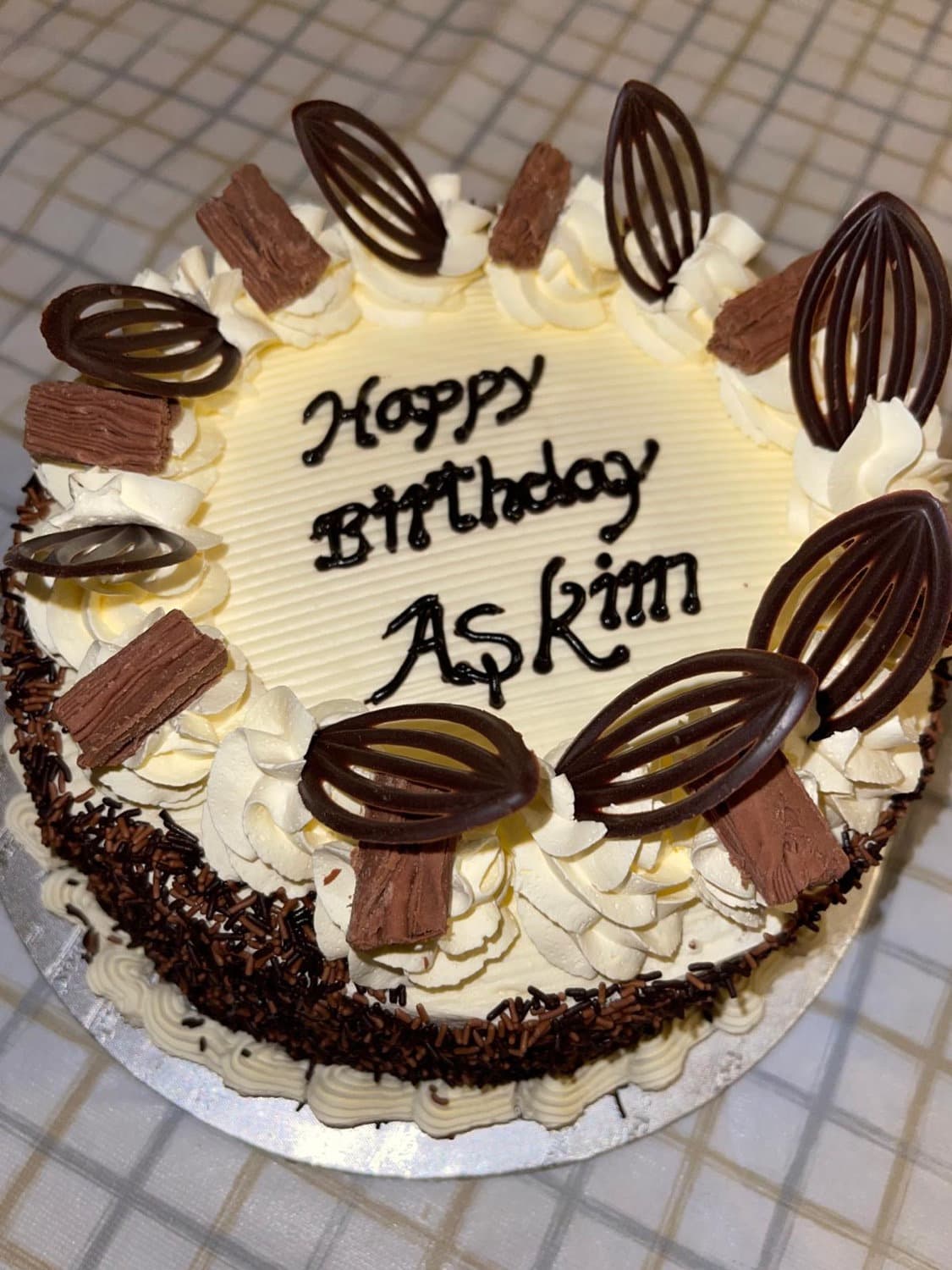 Cream birthday cake decorated with chocolate leaves and a handwritten message