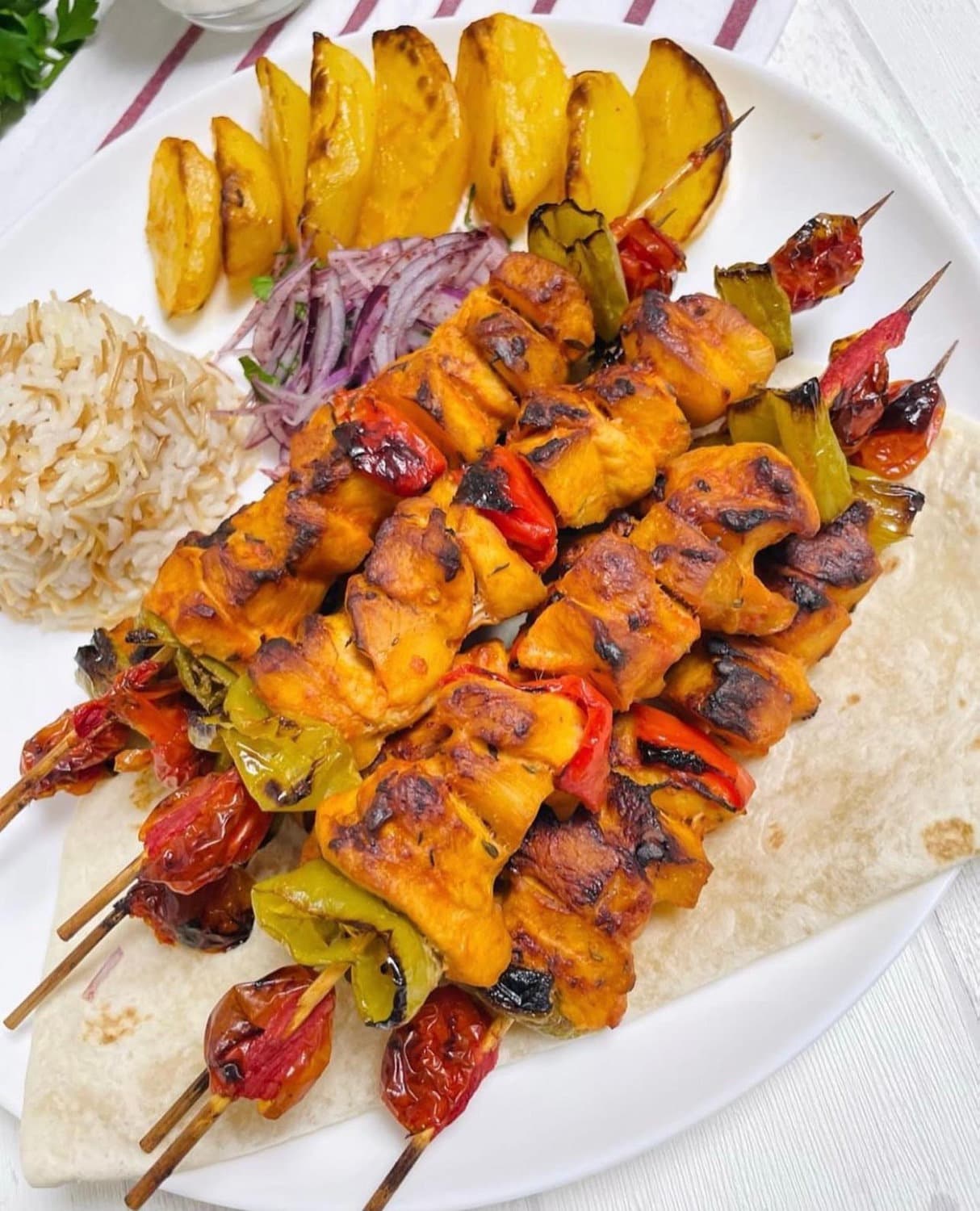 Chicken skewers with peppers and tomatoes, rice and potato wedges
