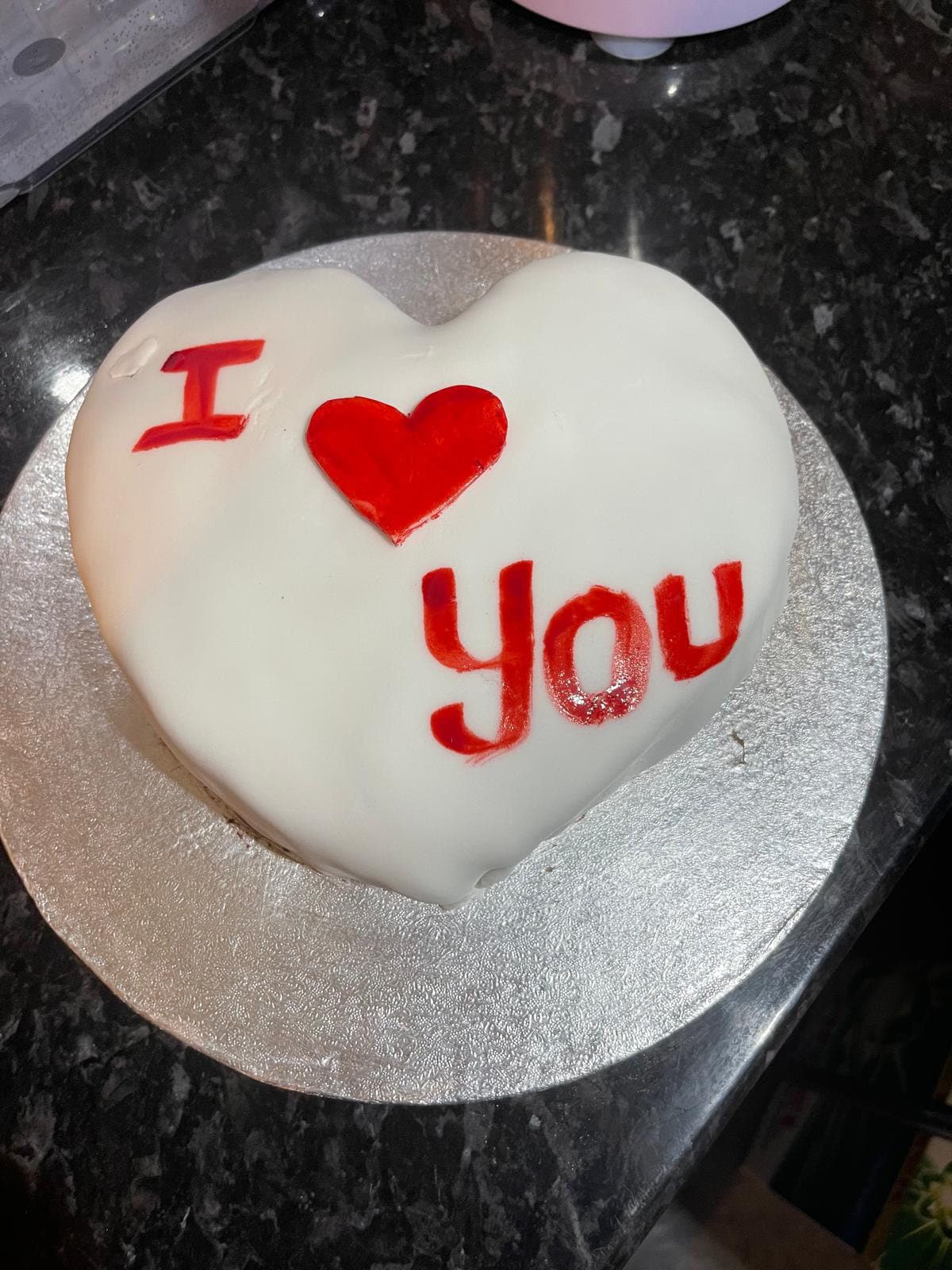 Heart-shaped white cake piped with I love you in red